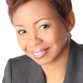 Training Series 4 A woman with short, reddish-brown hair smiles at the camera. She is wearing a dark blazer and light makeup, ready to present a Training Series, and is posed against a plain white background.