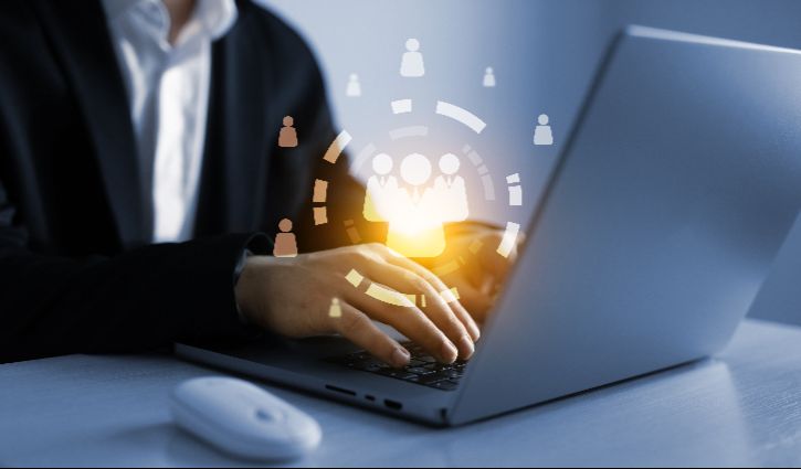 A person in business attire types on a laptop, with a glowing digital graphic of connected people icons above the keyboard, symbolizing networking or online communication. The scene evokes warm conversions from effective cold outreach. A wireless mouse is next to the laptop.