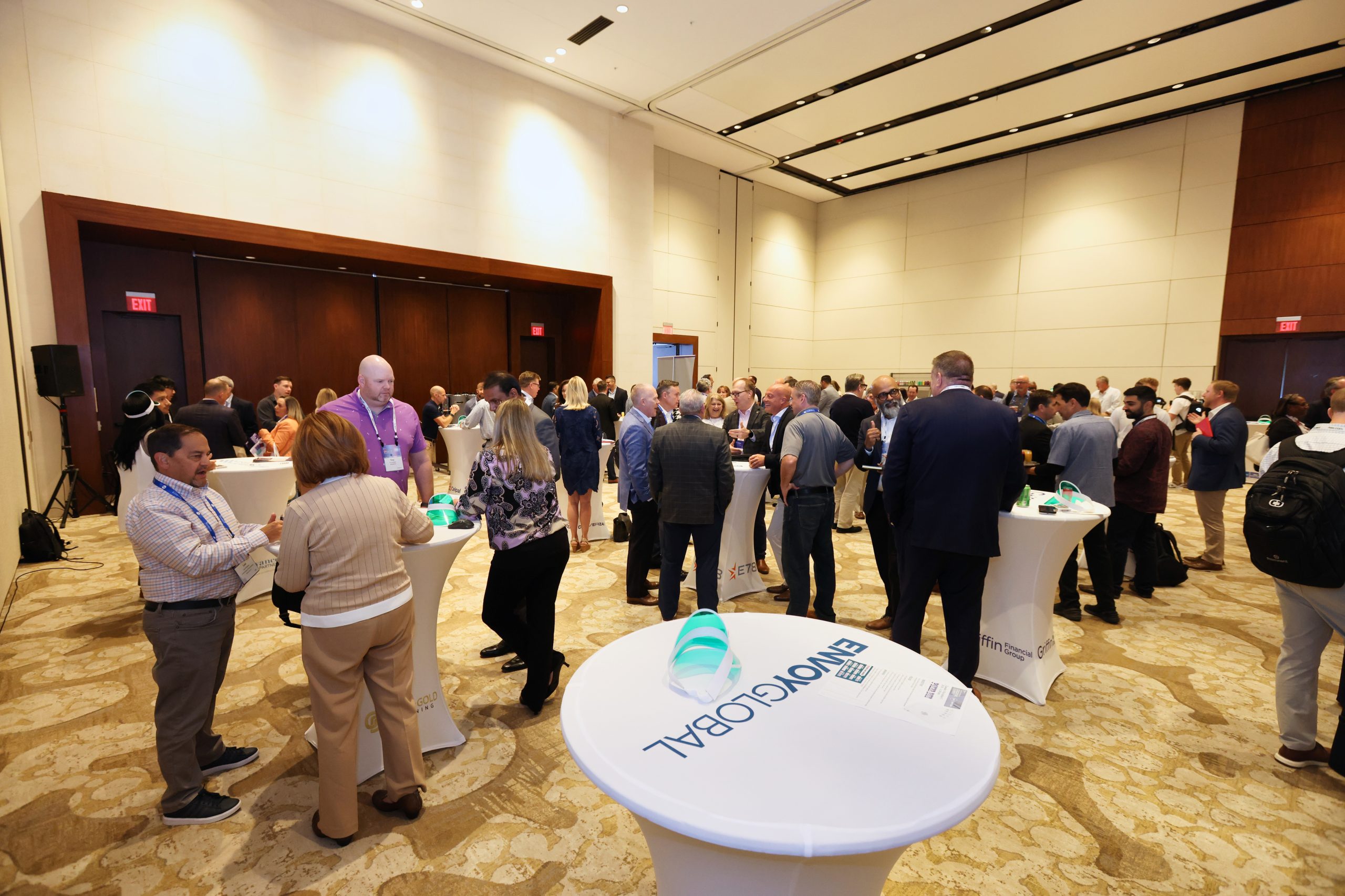 Executive Summit 15 A group of people mingles and networks around tall cocktail tables in a large, well-lit conference room with high ceilings and neutral decor. Branded materials with EINVOICING GLOBAL are visible on the tables.