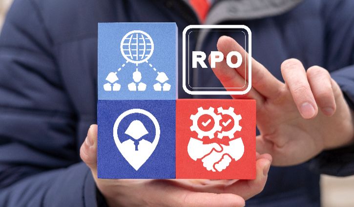 A person holds four cubes with icons—a globe with people, RPO in a square, a location marker with a helmet, and shaking hands with gears—symbolizing RPO Readiness and key concepts in Recruitment Process Outsourcing for the staffing business.