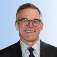 Bob Siemering, a middle-aged man wearing glasses, a dark suit, a striped shirt, and a striped tie, smiles warmly in front of a light blue gradient background.