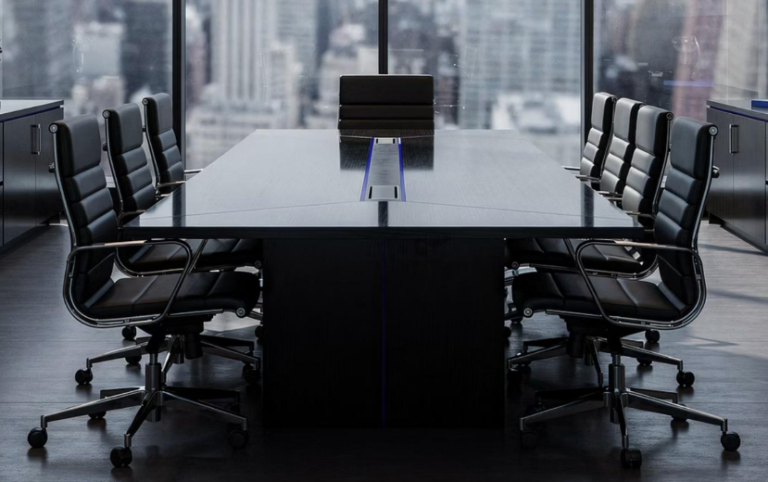 A modern, empty boardroom with a long black conference table, ten black chairs, and large windows overlooking a city skyline—an ideal setting for staffing leaders to share executive insights.