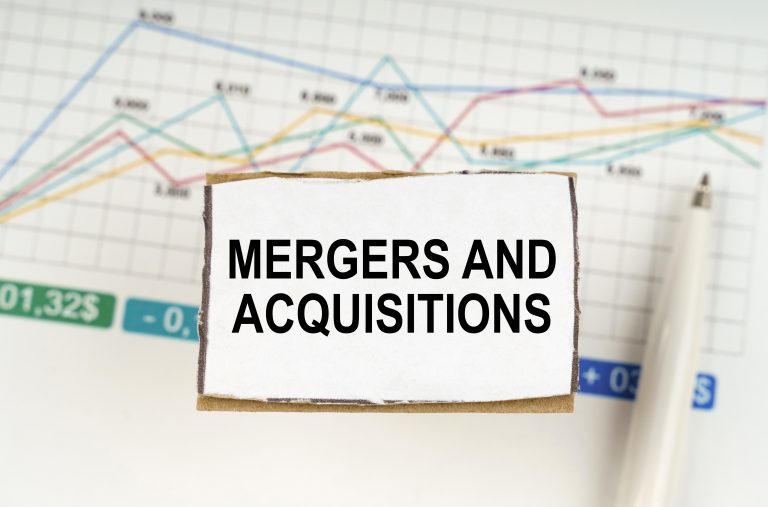 A sign reading Mergers and Acquisitions is displayed in front of a business chart with multicolored lines and a white pen placed on the side, highlighting the growing influence of firms like Impact Group IT in the TechServe M&A Marketplace.