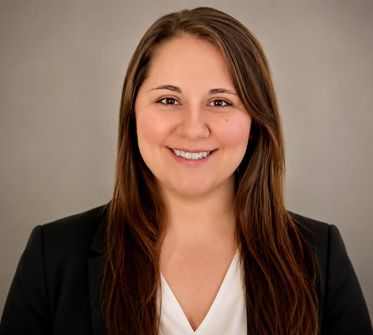Tiffany Boltz, a woman with long brown hair, smiles at the camera in a black blazer over a white blouse, posed against a plain, light gray background.