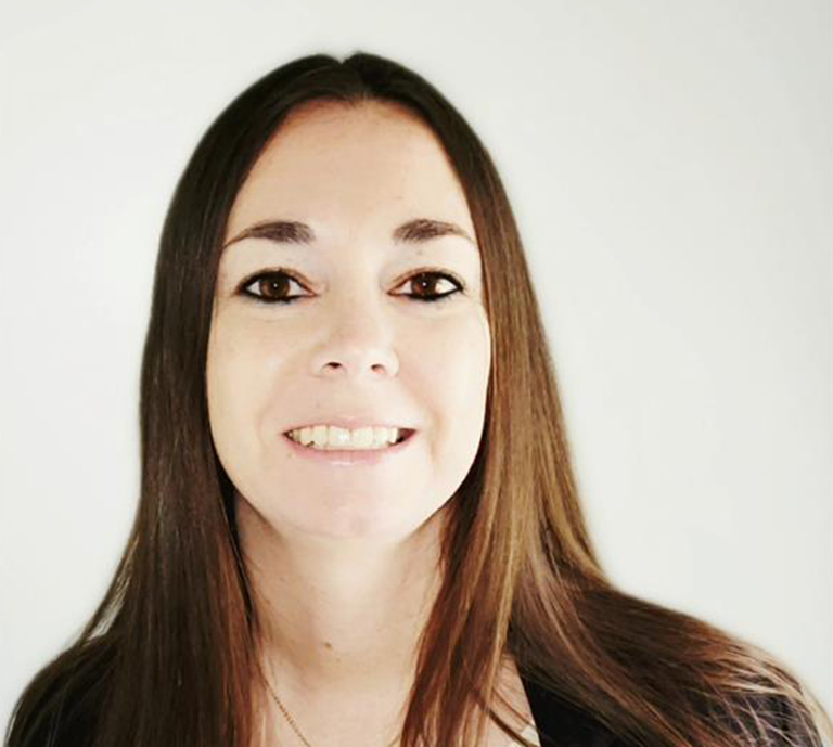 Tiffany Boltz, with long straight brown hair and dark eyes, is smiling at the camera against a plain white background. She is wearing a dark top.