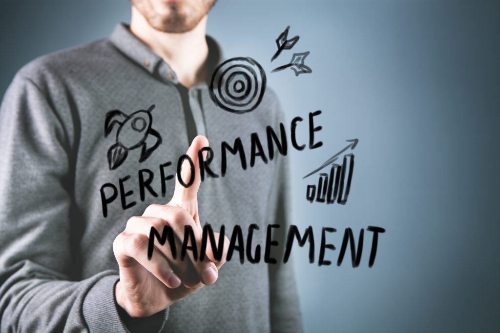 Rethinking Leadership: Why Performance Isn’t Enough 1 A person in a gray shirt points at a transparent screen displaying the handwritten words “performance management,” highlighting leadership with illustrations of a rocket, target, and upward graph.