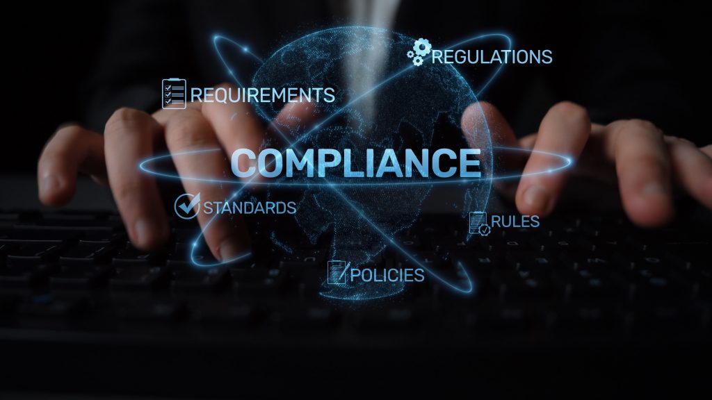 Preventing Worker Misclassification Risks Drives Competitive Advantage 1 Hands typing on a keyboard with the word COMPLIANCE and related terms like REQUIREMENTS, REGULATIONS, STANDARDS, RULES, and POLICIES digitally overlaid on a globe graphic—illustrating how addressing issues such as worker misclassification can provide organizations with a crucial competitive advantage in today’s global landscape.