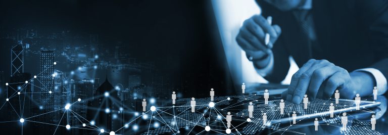 A person in a suit uses a tablet to manage IT staffing for a digital network of people icons overlaid on a nighttime cityscape.